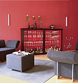 Hausbar hinter Glas im Holzregal vor Wand rot, kubische Möbel grau, Vasen