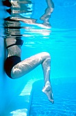 Woman wearing black lingerie performing abdominal and leg exercise in swimming pool