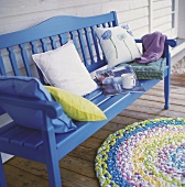 Blaue Holzbank mit farbigen Kissen, Becher + Zeitschrift auf der Veranda