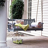 Swing with floral pattern cushions and fruits in wire basket on porch