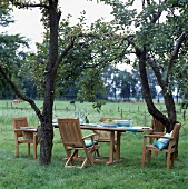 Gesdeckte Tafel auf der Wiese; Teak- Holz-Sitzgruppe unter Bäumen