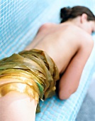 Semi nude woman lying with seaweed wrapped on her buttocks