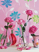 Blumenvasen mit Rosen vor geblümter rosa Tapete
