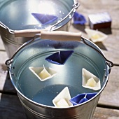 Close-up of zinc bucket of water and boat shaped candles floating