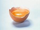 Broken brown egg shell with yolk and egg white on white background