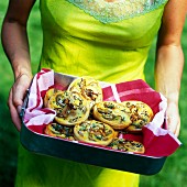 A woman carrying aubergine and potato tartlets in a baking tin