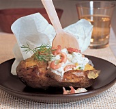 Baked potato with crayfish, cream and dill on a plate