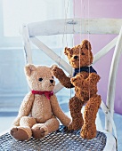 zwei Teddy-Bären, einer davon als Marionette, sitzen auf einem Stuhl