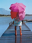 Frau, Rückenansicht, steht im Regen auf Bootssteg, Regenschirme, Stiefel