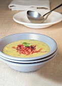 Potato and basil soup garnished with tomatoes and basil leaf in bowl