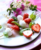 Strawberries with mozzarella on skewers with basil on plate
