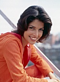 Portrait of young woman with dark hair wearing orange-red hooded jacket, smiling