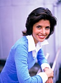 Portrait of pretty woman with dark hair wearing blue sweater leaning on railing, smiling
