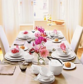 Gedeckter Tisch mit weißem Geschirr und Blumendekoration, schlicht