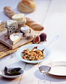 Plate of shrimp dish, cheese on wooden board with baguette and white wine on table