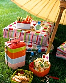 Stapelbare Lunchbox + bunte Polster- kissen unter Sonnenschirm