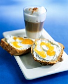 Cafe au lait in glass and slices of whole wheat bread topped with cottage cheese and jam