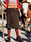 Woman wearing sweater, wrap skirt and boots standing in front of cow