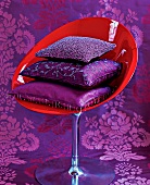 Stack of purple satin and silk cushions on red shell chair