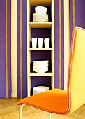 Orange chair in front of purple-orange striped wall with shelf