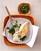 Cod on wooden spoon drizzled with caper pesto, overhead view