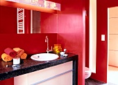 Interior of bathroom with white toilet seat, wash basin and red walls