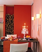 Candle lit dining table in front of red wall with alcove for firewood and wall lights