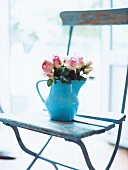 Rosenstrauß steht in einer blauen Kanne auf einem Holzstuhl
