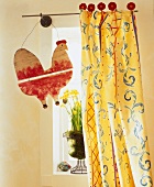 Yellow curtain in front of window with potted daffodils and wooden hen hanging