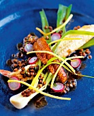 Close-up of lentil salad with smoked eel and onion sticks kept on blue plate