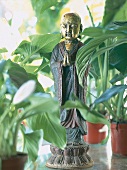 Glücksbringer, Buddha aus Gusseisen, bemalt, vor Topfpflanzen, close-up