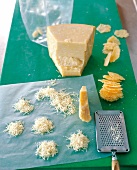 Grated and pieces of parmesan cheese with grater on green board