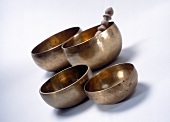 Close-up of four singing bowls and wooden clapper on white surface