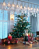 Candles, glasses and Christmas decorations on table with Christmas tree in background