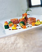 Saddle of rabbit wrapped in bacon and vegetables on skewers on plate