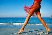 Close-up of woman wearing red cloth around her waist running on beach
