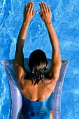 Rear view of woman lying on air mattress in pool, upward view