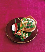 Asian salad in hollowed out coconut beside prawns and chili on banana leaf