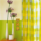 Hocker mit Vasen und Zierlauchblüte vor grün-weißer Wand, daneben grün-gelb karierte Gardine