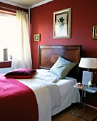 Edwardian bed with red cushion, blanket and painting on red wall