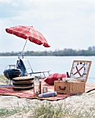 Picnic accessories, picnic basket and umbrella laid on picnic blanket at lake