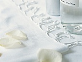 Close-up of towel with rose petals and bottles on white background