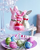 Homemade rabbit-shaped egg cosies and coloured eggs on a glass stand