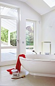 Bathroom with large windows, red towel on white bathtub and marble flooring