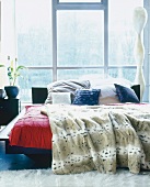 Bed with fur blanket and pillows in front of large window