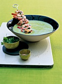 Bowl of pea cream soup with prawn skewer