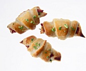 Close-up of small croissants with lamb salami cubes and chives on white background