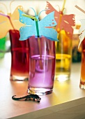 Close-up of butterflies from tracing paper on straws in colorful glass on table