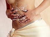 Woman scrubbing her belly with sea salt, mid-section