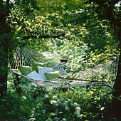 Width hammock with cushions hanging between two trees in garden